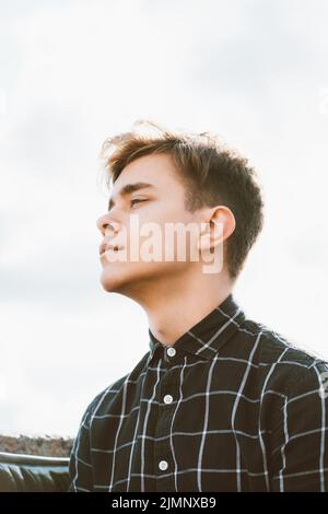 Porträt von jungen Kerl, brünett mit dunklen Haaren, kaukasisch. Nahaufnahme eines Jungen, eines Mannes, der an der Kamera vorbeischaut. Im Freien in der Stadt Stockfoto