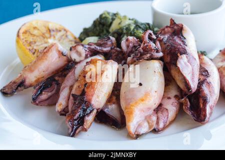 Gegrillter Tintenfisch mit Kartoffeln und Spinat auf einem weißen Teller. Gericht mit Meeresfrüchten. Romantisches Abendessen in einem Fischrestaurant im Ferienort Montenegro. Reisen Stockfoto