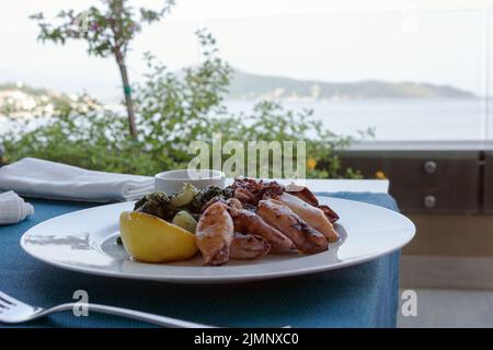 Gegrillter Tintenfisch mit Kartoffeln und Spinat auf einem weißen Teller. Gericht mit Meeresfrüchten. Romantisches Abendessen in einem Fischrestaurant im Ferienort Montenegro. Reisen Stockfoto