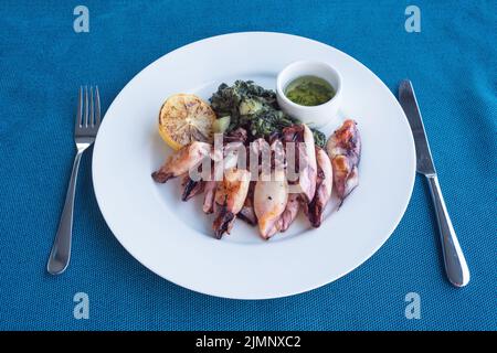 Gegrillter Tintenfisch mit Kartoffeln und Spinat auf einem weißen Teller. Gericht mit Meeresfrüchten. Romantisches Abendessen in einem Fischrestaurant im Ferienort Montenegro. Reisen Stockfoto