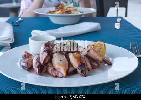 Gegrillter Tintenfisch mit Kartoffeln und Spinat auf einem weißen Teller. Gericht mit Meeresfrüchten. Romantisches Abendessen in einem Fischrestaurant im Ferienort Montenegro. Reisen Stockfoto