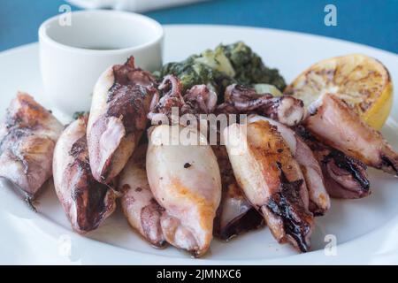 Gegrillter Tintenfisch mit Kartoffeln und Spinat auf einem weißen Teller. Gericht mit Meeresfrüchten. Romantisches Abendessen in einem Fischrestaurant im Ferienort Montenegro. Reisen Stockfoto