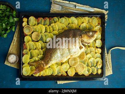 Gebackene Karpfen, ganze Fische aus dem Ofen mit Kartoffelscheiben auf einem großen Tablett traditionelle polnische Gerichte Stockfoto