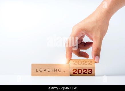 Wird auf 2023 Frohes neues Jahr. geladen Handumdrehung des 2022 bis 2023 Jahre Zahlenkalenders auf hölzernen Würfelblöcken isoliert auf weißem Hintergrund zur Vorbereitung Stockfoto