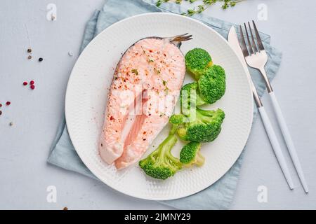 Dampflachs, Brokkoli, Paläo, Keto oder fodmap Diät. Weiße Platte auf blauem Tisch, Draufsicht Stockfoto