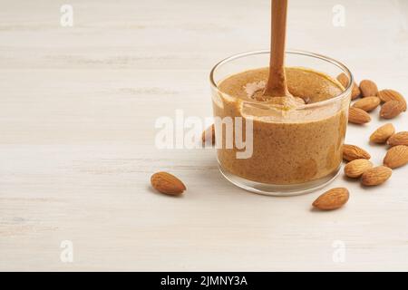 Mandelbutter, rohe Lebensmittelpaste aus gemahlenen Mandeln zu Nussbutter, knusprig und rühren, weißer Holztisch, Kopierraum Stockfoto