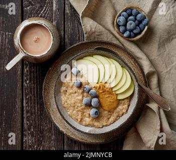 Haferbrei, gesunder Haferbrei in großer Schüssel mit Früchten und Beere zum Frühstück, Tasse Kakao. Stockfoto