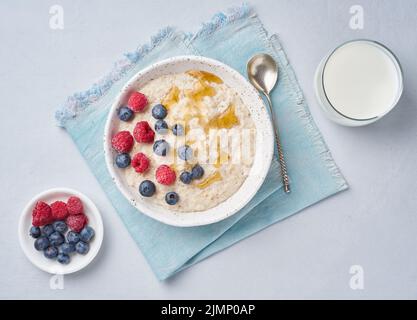 Haferflocken mit Beeren, Chia, Ahornsirup und einem Glas Milch auf blauem Hintergrund Stockfoto