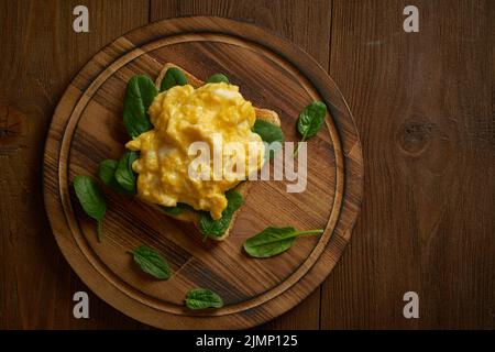 Toast mit Rührei und Spinat. Omelette. Frühstück mit gebratenen Eiern auf braunem dunklen Hintergrund. Draufsicht. Stockfoto