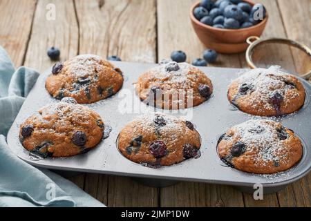 Blaubeer-Muffin im Tablett, Seitenansicht. Cupcakes mit Beeren in Backform auf alte Leinenserviette, rustikaler Holztisch, Frühstück wi Stockfoto