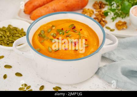 Karotten-Sahne-Suppe mit Kürbiskernen und Petersilie und Walnüssen, Seitenansicht auf hellem Hintergrund Nahaufnahme Stockfoto