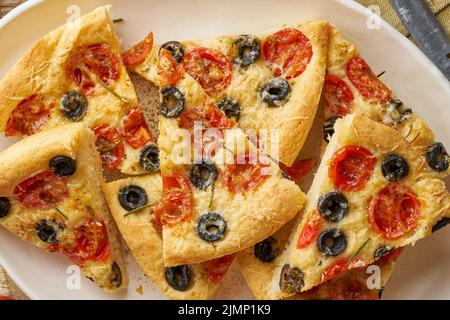 Focaccia, Pizza in Teller mit Tomaten, Oliven und Rosmarin. Gehacktes italienisches Fladenbrot Stockfoto