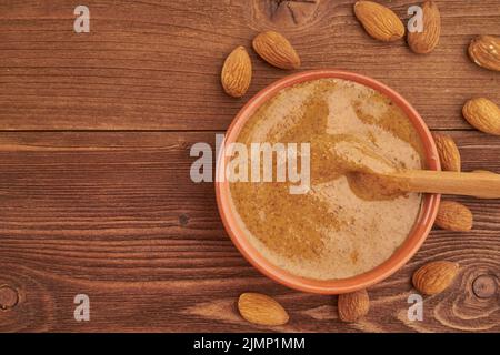 Mandelbutter, rohe Lebensmittelpaste aus gemahlenen Mandeln zu einer Nussbutter, knusprig und umrühren, dunkelbrauner Holztisch, Copy-ac Stockfoto