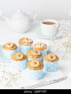 Bananenmuffin, Cupcakes in blauem Kuchenpapier, Seitenansicht, vertikaler, weißer Betontisch Stockfoto