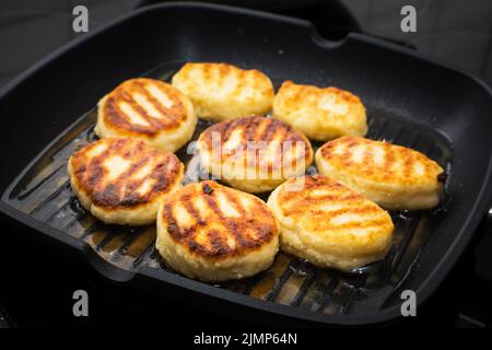 Traditionelle russische süße Syrniki-Hüttenkäse-Pfannkuchen in der Bratpfanne gebraten Stockfoto