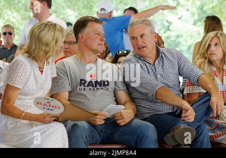 Fancy Farm, KY, USA. 06 August 2022. Der republikanische Kongressabgeordnete James Comer (zweiter von rechts) spricht mit Kelley Paul (links) und Rob Givens, dem Staatsdirektor von Senator Rand Paul, während seine Frau Tamara Comer (rechts) während des St. Jerome Fancy Farm Picnic 142. zuschaut. Das Picknick ist eine Spendenaktion für die katholische Kirche St. Jerome und bekannt dafür, dass es tonnenweise Grillfleisch serviert und politische Sprecher dazu einlädt, sich vor einer Menschenmenge, die zum Zwischenruf zugelassen und ermutigt wird, gegenseitig zu amüsieren. (Kredit: Billy Suratt/Apex MediaWire über Alamy Live News) Stockfoto