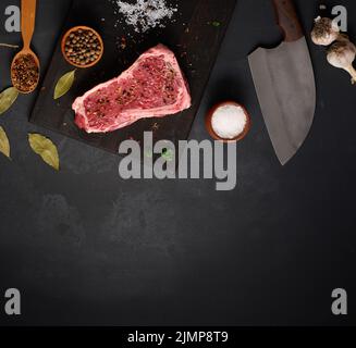 Frisches rohes Stück Rindfleisch, Striploin-Steak auf schwarzem Hintergrund, Draufsicht. Marmoriertes Stück Fleisch Stockfoto