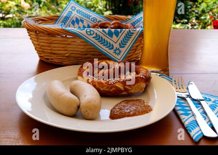 Ein traditionelles bayerisches Gericht: Weiße Würstchen, knusprige, salzige Brezeln, serviert mit süßem Senf und köstlichem deutschen Bier und einem Korb Stockfoto