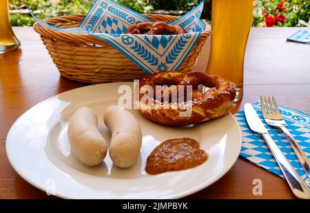 Ein traditionelles bayerisches Gericht: Weiße Würstchen, knusprige, salzige Brezeln, serviert mit süßem Senf und köstlichem deutschen Bier und einem Korb Stockfoto