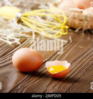 Raw organic Braun huhn eier mit Eigelb Weidenkorb und Schneebesen auf Küche aus Holz Tisch gebrochen Stockfoto