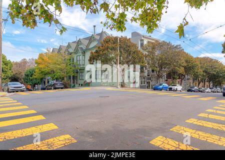 Kreuzungsstraße mit gelben Fußgängerzonen in den Vororten von San Francisco, Kalifornien. Es gibt einen Blick auf Stadthäuser mit grünem Äußeren mit Veh Stockfoto