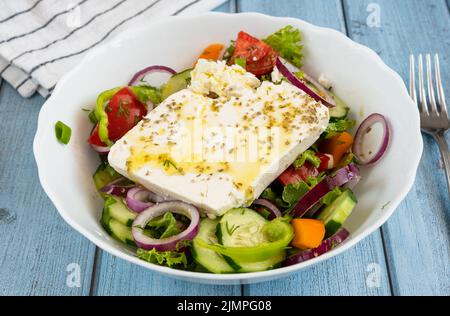 Traditioneller griechischer Salat mit einem großen Stück Feta-Käse, Gemüse, Orangen und Olivenöl Stockfoto