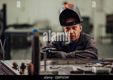 Professioneller Schweißer für die Schwerindustrie, der in der Fabrik arbeitet, trägt Helm und beginnt zu schweißen. Selektiver Fokus Stockfoto