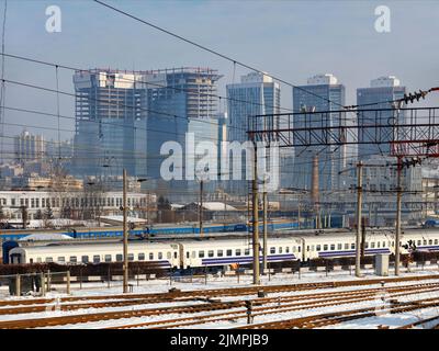 Elektrische Hochspannungsleitungen auf Stahlbeton- und Metallmasten vor der Kulisse eines Bahnhofs und von Wolkenkratzern der Stadt an einem Wintertag. Stockfoto