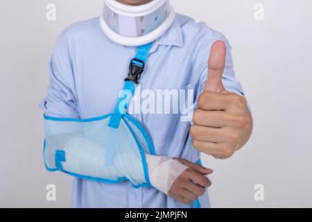 Porträt eines asiatischen Mannes mit gebrochenem Arm und Hals Gefühl zeigt Daumen nach oben Geste isoliert auf weißem Hintergrund Kopie Raum Stockfoto