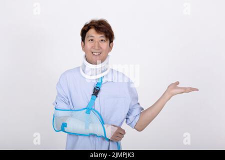 Porträt eines lächelnden asiatischen Mannes mit gebrochenem Arm und Hals zeigt leeren Raum isoliert auf weißem Hintergrund Kopie Raum für Text Stockfoto