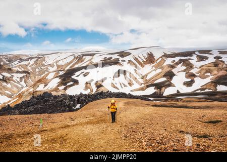 Majestätischer Blick vom Brennisteinsalda Trail mit weiblicher Wanderung auf vulkanischem Berg und schneebedecktem Landmannalaugar im Hochland von Island Stockfoto