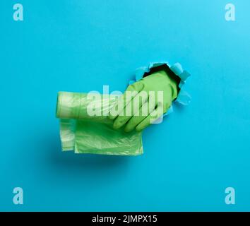 Die Hand hält ein Paket transparenter Müllbeutel auf blauem Hintergrund. Ein Teil des Körpers ragt aus einem zerrissenen Loch im Papier heraus Stockfoto