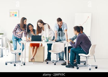 Lächelnde, vielfältige Gruppe junger Menschen, die im Büro zusammenarbeiten und miteinander kommunizieren Stockfoto