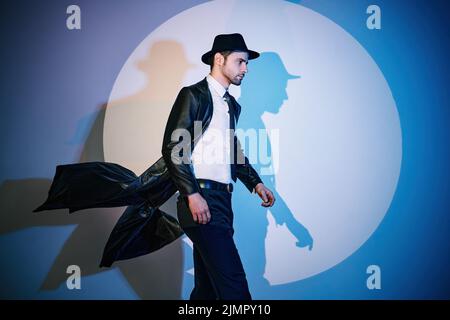 Schöner Mann in schwarzem Mantel und Hut, der wie ein Superheld im Rampenlicht steht Stockfoto