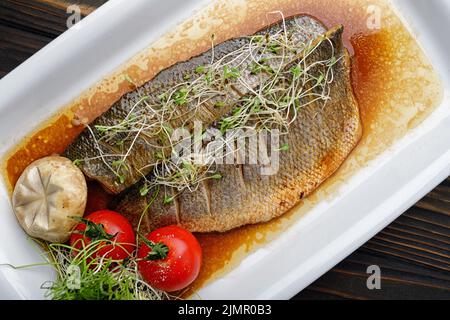 Dorado Fischfilet in Sauce gegrillt, mit Tomaten auf einem Teller auf einem Holzboden Stockfoto