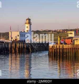 Am frühen Morgen erleuchtet die Sonne den Leuchtturm am Eingang zum Hafen von Scarborough an der Küste von North Yorkshire. Stockfoto