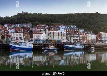 Fischerboote vertäuten im Hafen von Scarborough, mit Scarborough Castle im Hintergrund. Stockfoto