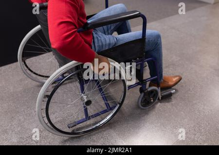 Niedriger Teil des jungen afroamerikanischen behinderten Geschäftsmannes im Rollstuhl am Arbeitsplatz Stockfoto