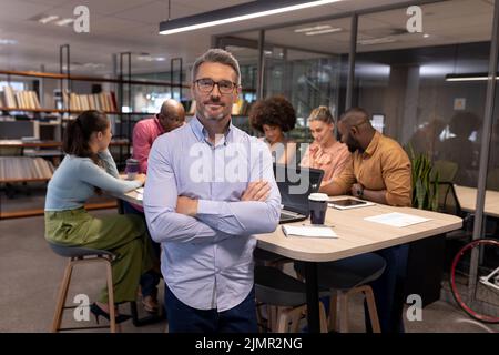 Porträt eines reifen kaukasischen Geschäftsmannes, der mit gekreuzten Armen gegen biracial Kollegen steht Stockfoto