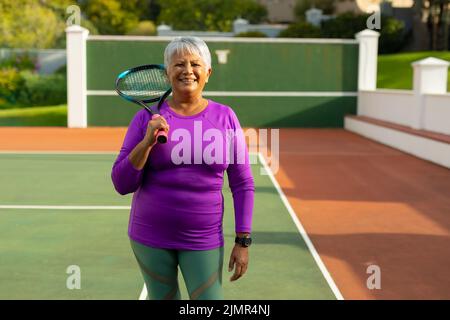 Porträt einer selbstbewussten, lächelnden älteren Frau aus der Birazialzeit mit kurzen Haaren und Tennisschläger auf dem Tennisplatz Stockfoto