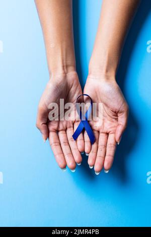 Beschnittene Hände einer afroamerikanischen Frau mit mittlerem Erwachsenen mit blauem Band auf blauem Hintergrund Stockfoto