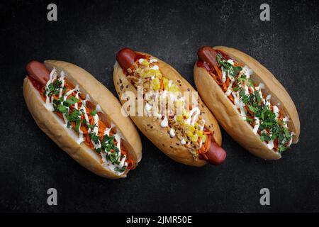 Drei Hotdogs mit verschiedenen Füllungen und verschiedenen Würsten auf grauem Beton Stockfoto