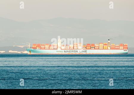 RIJEKA, KROATIEN - JULI 10 2022: Containerschiff fährt auf tiefblauem Ozean. Weißes Schiff transportiert Container am 10. Juli in Rijeka gegen den trüben Berg an der Küste und den bewölkten Himmel Stockfoto