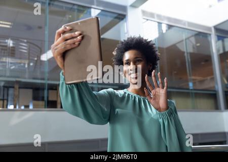 Lächelnde afroamerikanische Geschäftsfrau winkt bei Videoanruf über Tablet-pc am Arbeitsplatz Stockfoto