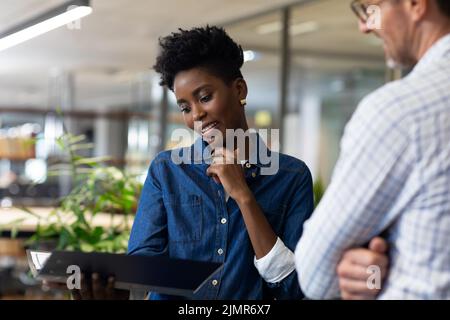 Lächelnde afroamerikanische Geschäftsfrau, die am Arbeitsplatz mit einem kaukasischen Geschäftsmann über die Akte diskutiert Stockfoto