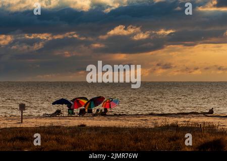 Auf einem Strand auf Dauphin Island, Alabama, werden farbenfrohe Sonnenschirme unter einem dramatischen Himmel in einem zusammengesetzten Bild aufgestellt. Stockfoto