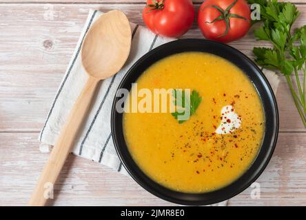 Rote Linsenpüree-Suppe auf einem Teller mit einem Holzlöffel. Stockfoto