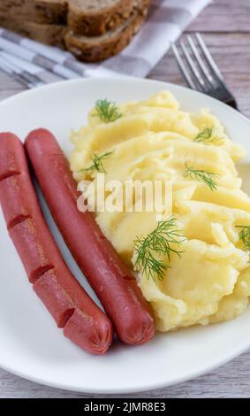 Kartoffelpüree auf einem Teller und ein paar Würstchen auf einem Holzhintergrund. Stockfoto