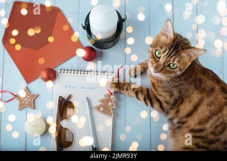 Ein Brief an den Weihnachtsmann, ein Umschlag, Weihnachtsspielzeug und eine Katze auf einem Holztisch. Stockfoto
