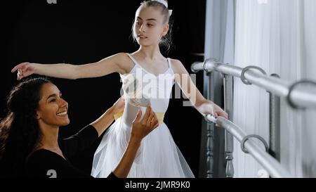 Mädchen Teenager Ballerina Schüler tun klassische Übungen in der Nähe von Ballett Barre Züge hört auf Rat der Frau Lehrer professionelle weibliche Trainer hilft Stockfoto